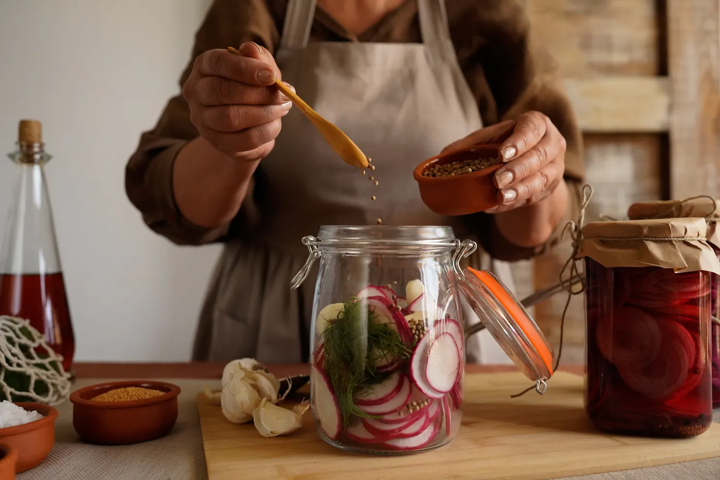 Hände geben Gewürze zu Radieschen in ein Fermentationsglas
